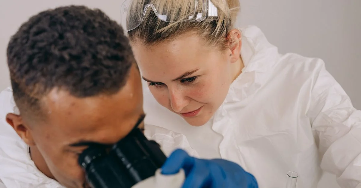 Deux scientifiques en tenue de laboratoire effectuent des recherches microscopiques, mettant l'accent sur la collaboration et la précision.