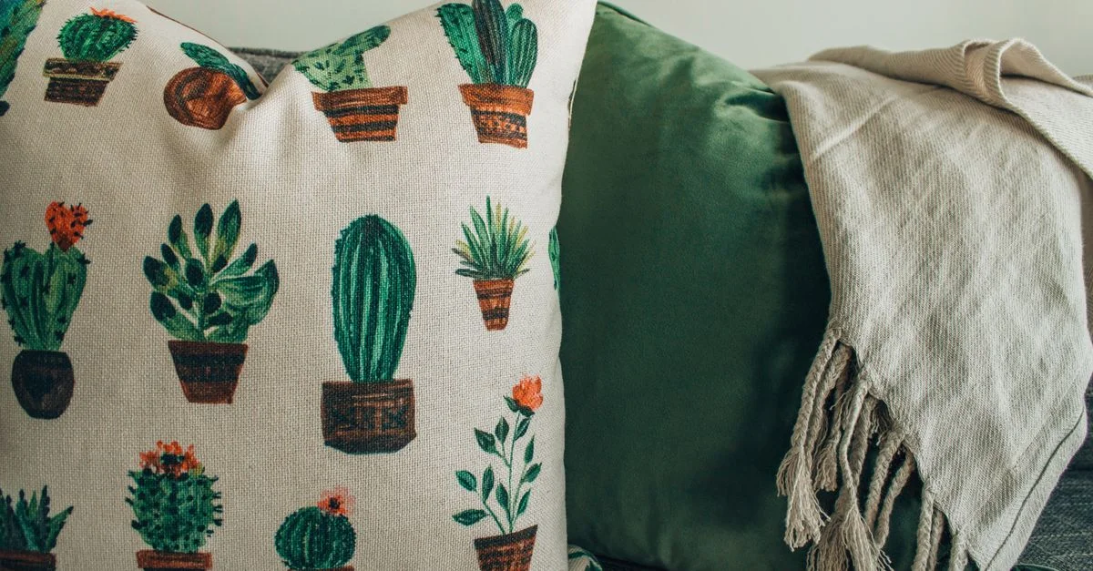 Un intérieur moderne et cosy avec des coussins imprimés de cactus et une douce couverture sur un canapé.