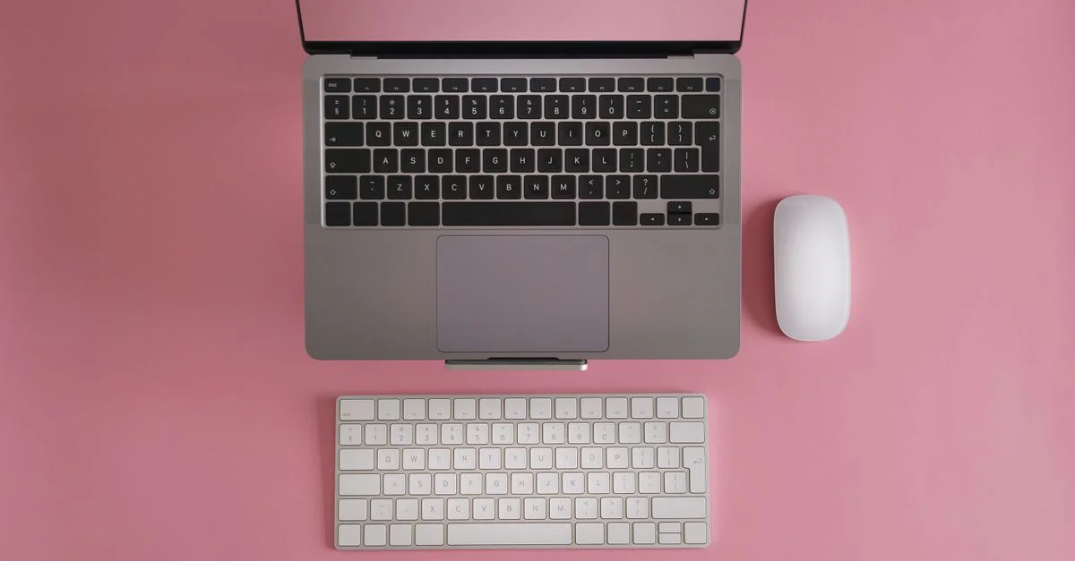 Vue de dessus d'un ordinateur portable, d'un clavier et d'une souris sur une surface rose. Parfait pour du contenu technologique.