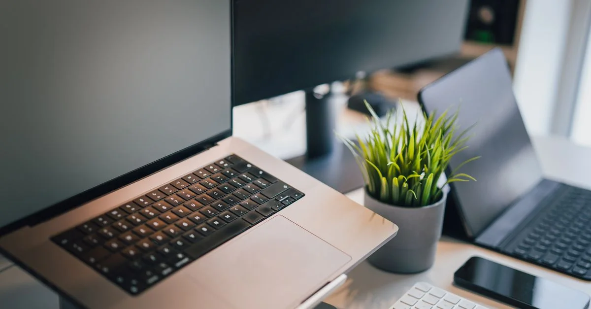 Un espace de travail de bureau élégant avec un ordinateur portable, un smartphone, un clavier et une plante en pot pour la productivité.