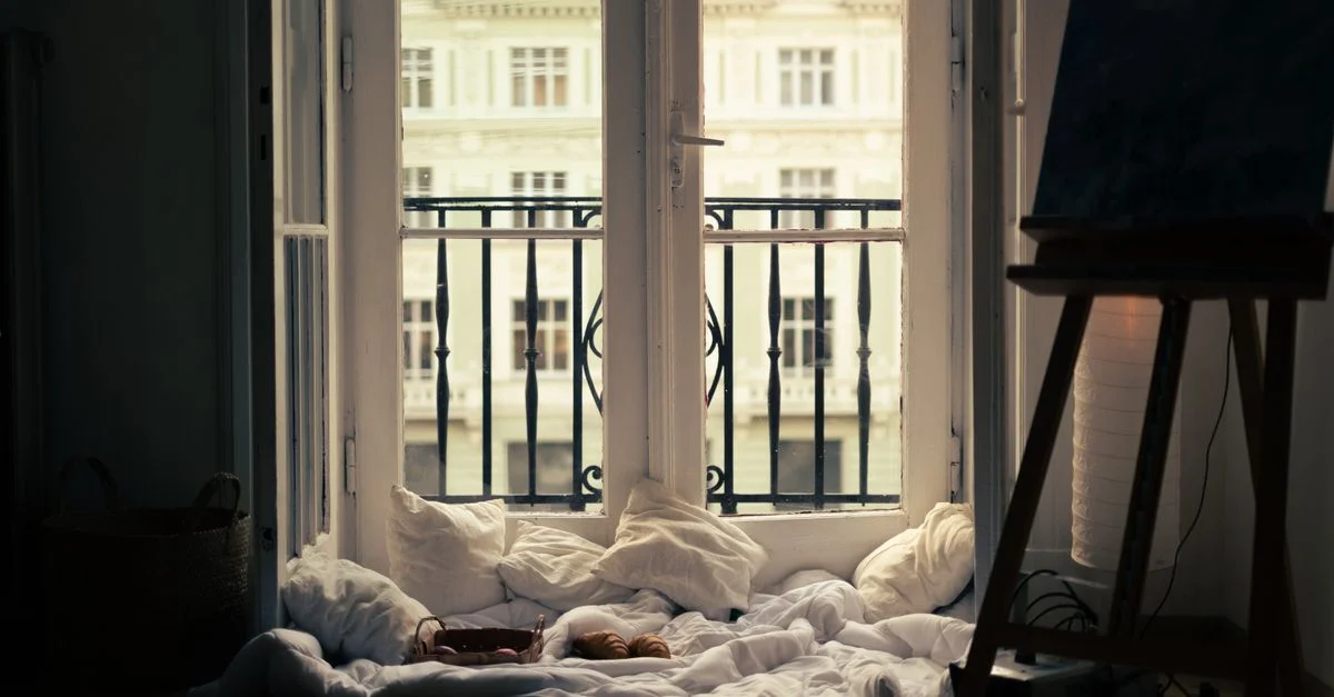 Une scène intérieure confortable avec des coussins près d'une fenêtre de balcon, surplombant une architecture classique.