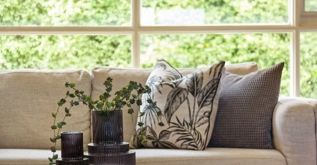 Salon élégant en gros plan mettant en valeur un sofa moelleux avec des coussins et un vase en verre dans un espace lumineux.